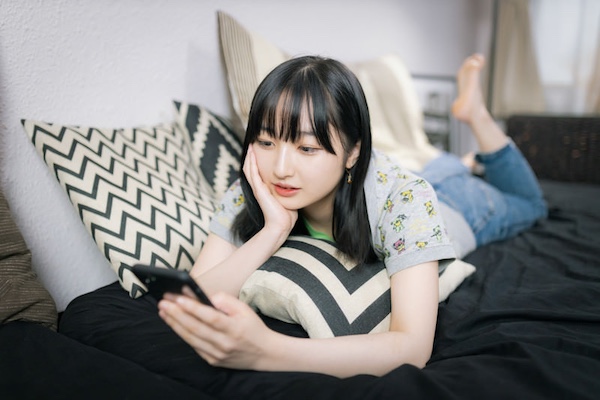 :ソファーで寝転ぶスマホ女子の無料の写真素材