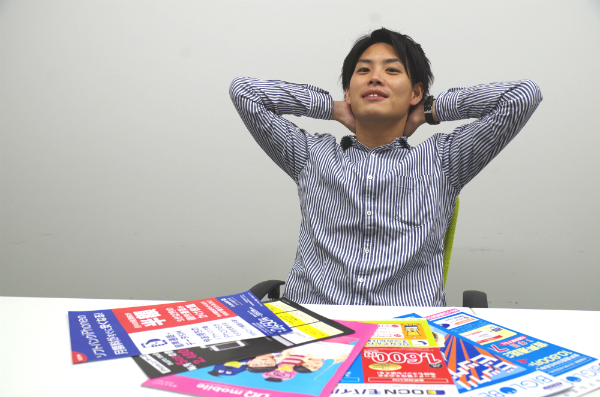 格安SIMのチラシとパンフレットの山を前にドヤ顔。これだけの量を良く集めた、すごいぞタッツミーくん